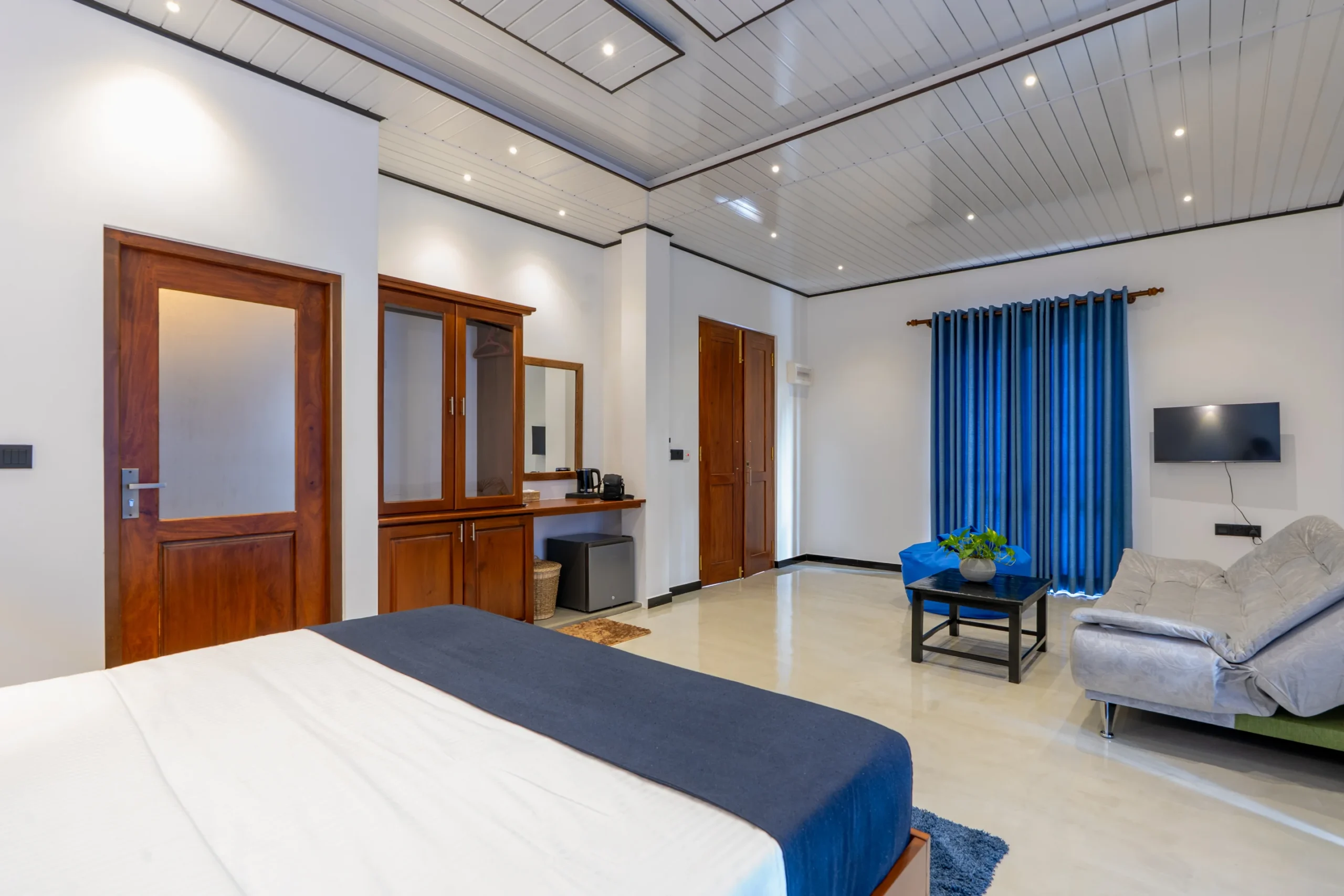 Spacious hotel room with wooden furniture, modern ceiling lights, and blue décor